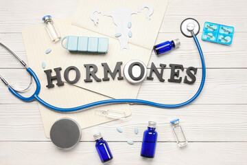 Word HORMONES with medications, notebooks and stethoscope on white wooden background