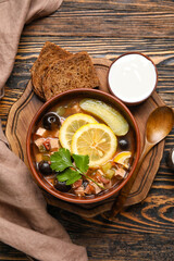 Bowl of tasty Hodgepodge soup with sour cream and bread on wooden background