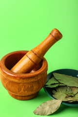 Wooden mortar and pestle with bay leaves on green background