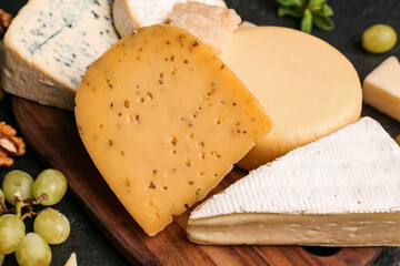 Wooden board with different types of tasty cheese on dark background, closeup