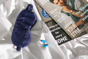 Sleeping mask with magazines and earplugs on bed