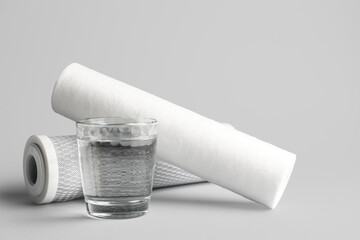 Glass of liquid and water filter cartridges on grey background