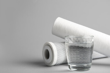 Glass of liquid and water filter cartridges on grey background