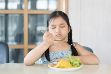 Asian child or kid girl unhappy and don't like eating vegetables salad with corn tomato and greens...