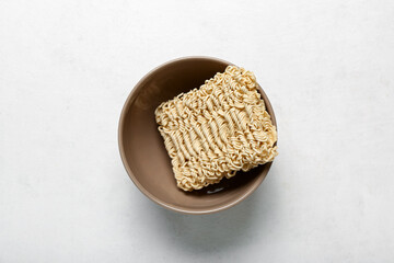 Raw instant noodles in bowl on white grunge background