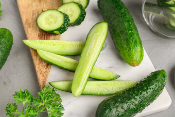 Board with fresh cut cucumbers on grey background