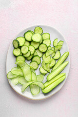Plate with fresh cut cucumber on light background