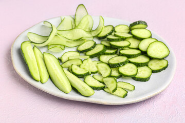 Plate with fresh cut cucumber on light background