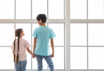 Little boy with his sister holding hands near window