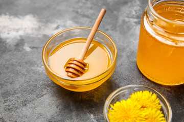 Jar and bowl with dandelion honey on dark grunge background