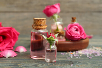 Bottles of cosmetic oil with rose extract and flowers on wooden table