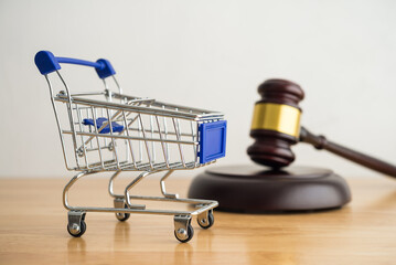 Shopping trolley cart and hammer judge gavel on wooden table with white wall background copy space....