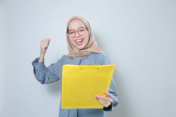 Happy beautiful young Asian muslim business woman wearing glasses holding clipboard over isolated background