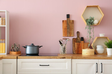 Electric stove with cooking pot and utensils on kitchen counter near pink wall