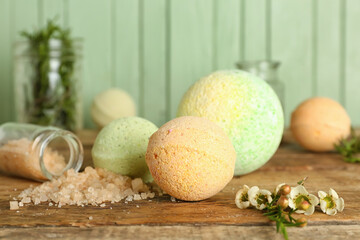 Bath bombs with flowers and sea salt on wooden table, closeup