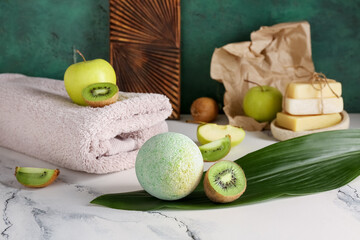 Spa composition with bath bomb, kiwi and tropical leaf on table