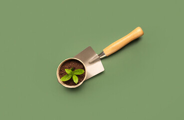 Peat pot with green seedling and shovel on green background - obrazy, fototapety, plakaty