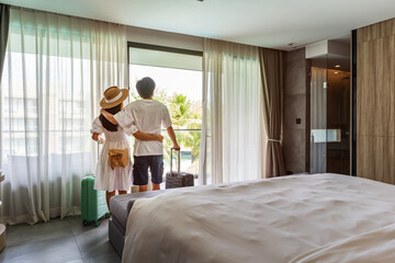 Young couple traveler opening the curtains and looking at the view from the window of a hotel room while on summer vacation, Travel lifestyle concept - 600037669