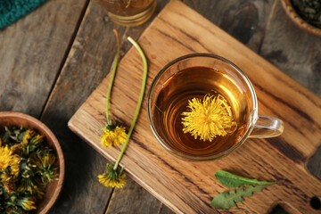 Board with glass cup of healthy dandelion tea on wooden table
