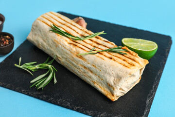 Board with tasty shawarma and rosemary on blue background