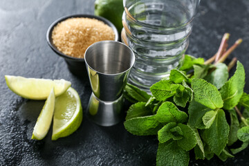 Glass, measure cup and ingredients for preparing mojito on dark background