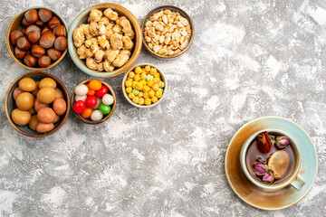 Fototapeta na wymiar top view hazelnuts and peanuts with candies and cup of tea on white background nut hazelnut walnut snack candy