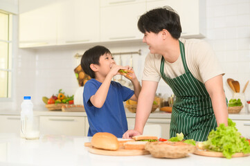 Obraz na płótnie Canvas Happy Young Asian father making breakfast to his son in kitchen at home