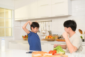 Obraz na płótnie Canvas Asian boy showing strong arm , playful with his father in home
