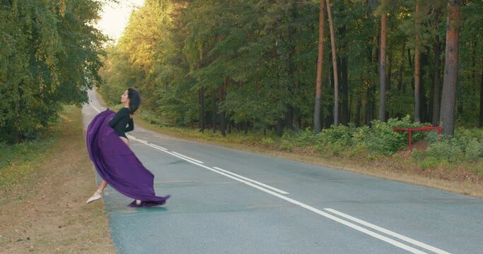 beautiful brunette girl dancer jumping on road. gymnast doing splits in air against blue sky. freedom to jump in sunny weather. gymnastic twine. young ballerina in black body suit performs split jump