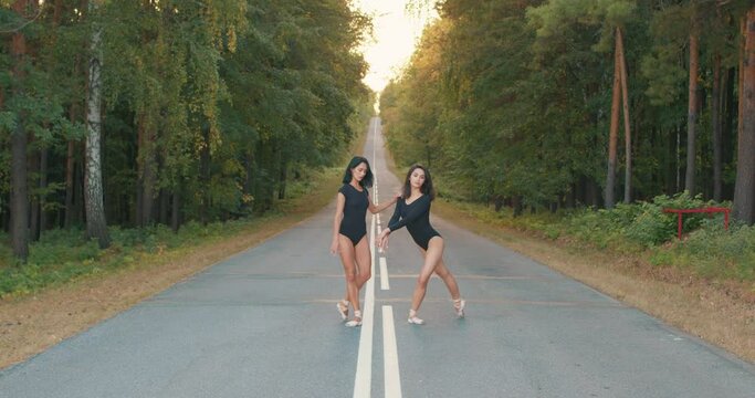 flexible awesome good-looking women in black bodysuit moving elegantly. ballet, dance concept. Professional ballerina ladies dancing in forest on road. female tenderness and freedom