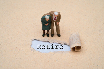 Couple miniature figure senior pensioners man and woman standing with retire wording on brown punch...