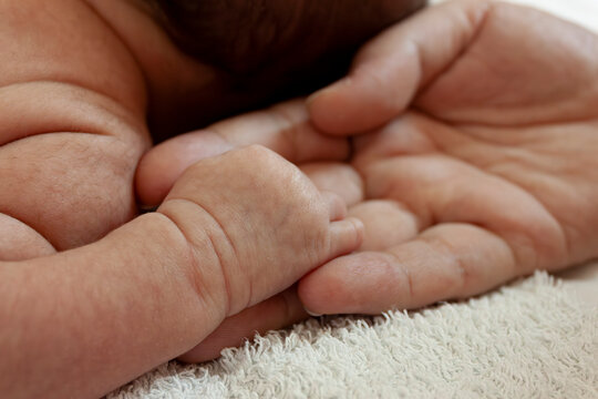 A father holding a tiny newborn baby's hand gently