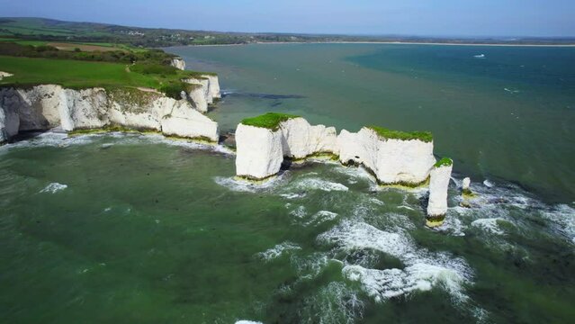 High wide aerial shot circling around Old Harry Rocks, limestone stacks on Dorset coastline, rough seas and big waves. UK