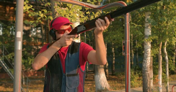 young man dressed in casual t-shirt, cap, protective eyeglasses headset killing birds, hunter is practicing with gun in a shooting range for improving self-defense technique with gun Skeet Shooting