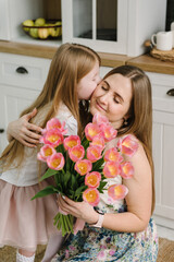 Daughter congratulates mother and gives bouquet of tulip flowers in kitchen at home. Mother's day...