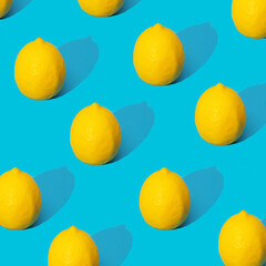 Juicy yellow lemons on a blue background with hard shadows. Summer pattern with ripe lemons. 