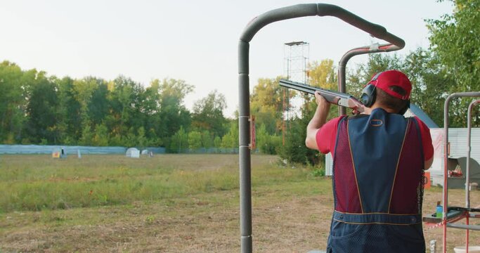 Skeet Shooting Sport. Rear View of Young Experienced Male wear Ear Plug Confidently Aiming Shotgun At Target in Outdoor Shooting Range, Alone. Man Practicing Fire Weapon Shooting. Hobby, Skill