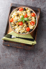Vegetarian millet porridge with fried eggplant, onions, tomatoes and basil close-up in a bowl on the table. Vertical top view from above