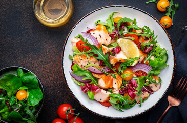 Gourmet salad with grilled salmon with tomatoes, cucumber, arugula, radicchio, red onion and lettuce with lemon oil dressing. Healthy lunch. Brown stone table background, top view