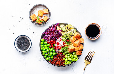 Healthy vegan food. Buddha bowl with quinoa, fried tofu, avocado, edamame, green peas, radish, cabbage and sesame seeds. White kitchen table background, top view