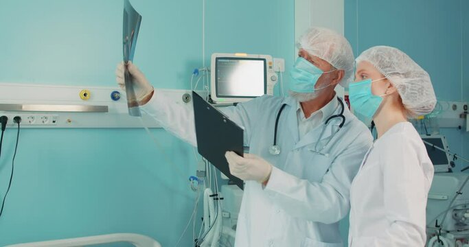 Competent medical professionals old man and young woman discussing and showing patient's lungs scan. Senior male doctor talking to young female nurse holding x-ray Medicine, healthcare concept.