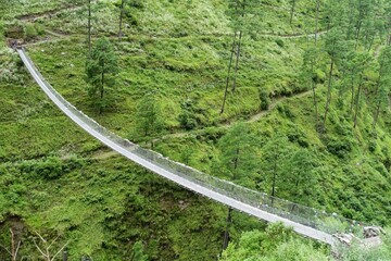 A suspension bridge viewed from a high angle on the Manaslu Circuit trek in Nepal, adding to the natural beauty of a tranquil rainforest rich with lush foliage and growth in the Himalayas. 