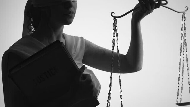 Woman standing blindfolded with a hand scale in one hand and a folder in the other. Image of the Themis as a concept of fair and unbiased justice