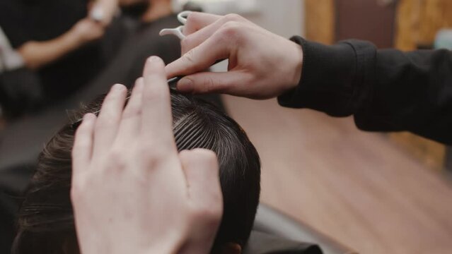 Professional barber carefully combing client close up before starting a haircut. Barber's hands with comb and scissors divide the hair of a man into zones for cutting in a barbershop