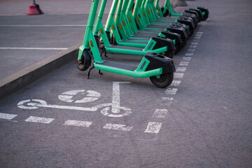 Green electric rent bikes parked in electric scooters parking area, marked with spray paint. Dedicated electric scooter parking spot on city sidewalk. 