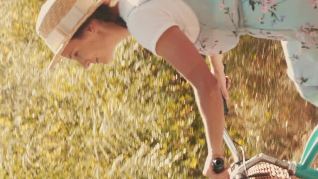 Cheerful female in straw hat riding retro bicycle at summer. Vertical video