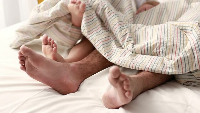 Closeup cropped video of of loving couple's feet, man and woman play their feet under blanket while wake up in bed in morning, girl puts her legs on husband slow motion. couple rest at weekend