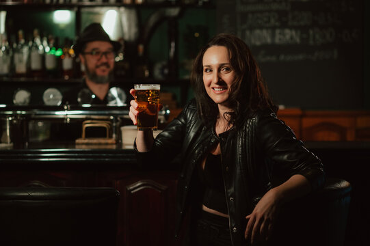 happy woman with a glass of light draft beer lager at bar counter in a pub