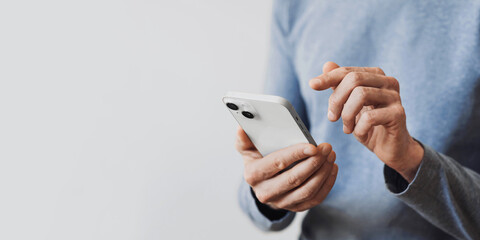 Young man texting on smartphone over gray background. Close up of adult male hand using mobile phone, panoramic banner with copyspace
