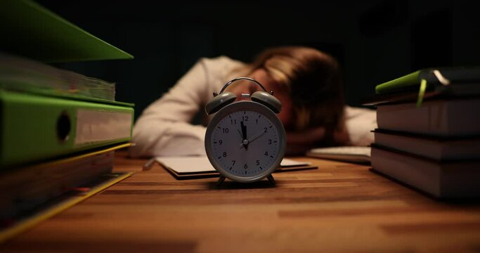 Business woman sleeping at the table with an alarm clock in office late at night. Overtime deadline and overwork